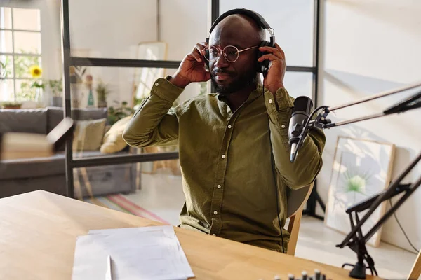 若いアフリカ系アメリカ人の男は 局所主題に関する彼の推測でオーディオファイルを記録する準備をしながらヘッドフォンをかける — ストック写真