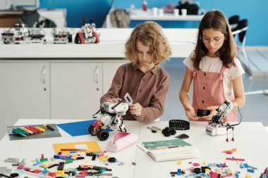 Robotun parçalarını birbirine bağlayan günlük giyimde iki zeki sınıf arkadaşı, robot bilimi dersinde yeni bir elektronik oyuncak modeli oluşturuyorlar.