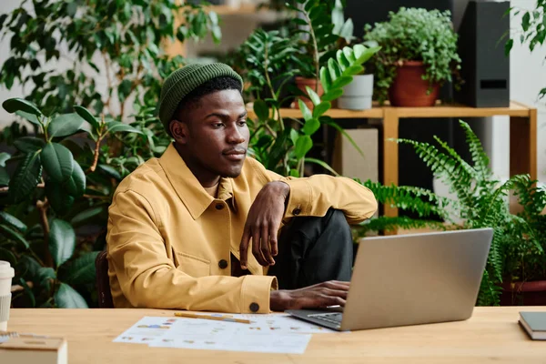 身穿便服的年轻而严肃的黑人男子坐在工作场所的绿色办公室笔记本电脑屏幕前 为商业项目工作 — 图库照片