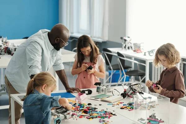 stock image Group of youthful learners constructing new robots at lesson with teacher advice and help while connecting parts of toys together