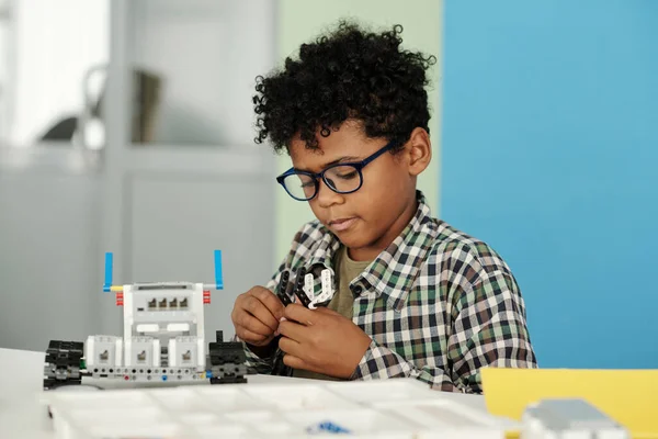 Chytrý Chlapeček Neformálním Oblečení Brýlích Spojující Detaily Hračkářského Robota Zatímco — Stock fotografie