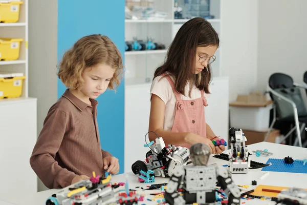 stock image Side view of two pupils standing by table with equipment for robot constructing and connecting details together at lesson