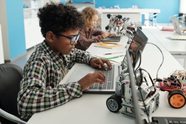Zeki Afrikalı Amerikalı öğrencilerin ders sırasında dizüstü bilgisayarın önünde oturup proje için çevrimiçi bilgi arayışının yan görüntüsü