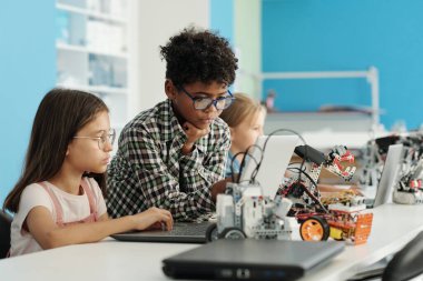 İki sevimli kültürler arası sınıf arkadaşı ders sırasında dizüstü bilgisayar ekranına bakıyor ya da yeni robot modelinin sunumunu hazırlıyorlar.