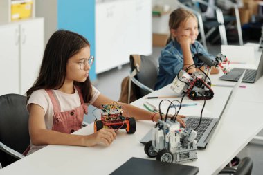 Akıllı öğrenci elektronik dokümana bilgi giriyor ve oyuncak robotu tanımlarken dizüstü bilgisayar ekranına bakıyor.