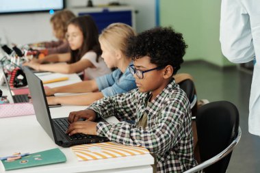 Sırayla dizüstü bilgisayarların önünde oturan Afro-Amerikan öğrenci ve sınıf arkadaşlarının yan görüntüsü.