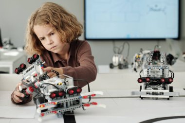 Zeki genç öğrenci robotik dersinde masanın başında oturuyor ve tüm detayları bir araya getirirken oyuncak robot yapıyor.