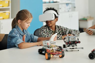 VR kulaklıklı yakışıklı okul çocuğu kafasını tablet ayarlama ayarlarıyla sınıf arkadaşına çeviriyor. Sanal oyun veya sunum ayarları.