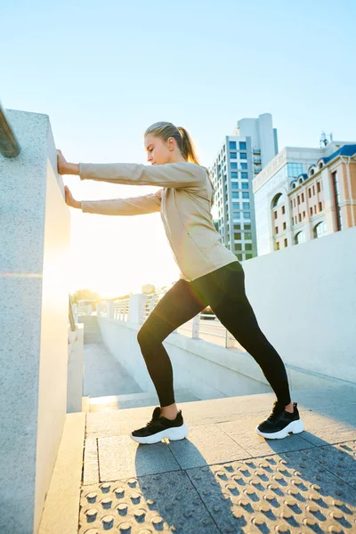 都市環境で物理的な運動をしながら 橋のフェンスによって保持活動中の若いブロンドのスポーツ女性の側面図 — ストック写真