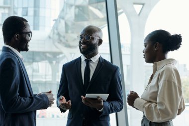 Formalite icabı giyinmiş üç genç Afrikalı Amerikalı çalışandan oluşan bir grup yeni iş projesine hazırlanırken fikir alışverişinde bulunuyorlar.