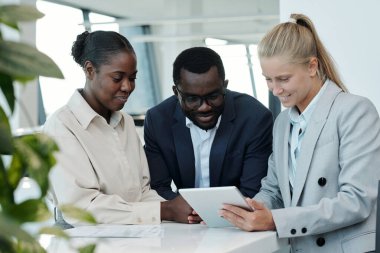 İş toplantısında mali verileri tartışırken, resmi giyim sektöründe çalışan bir grup genç yönetici tablet ekranına bakıyor