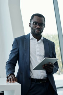 Kendine güveni tam bir borsacı ya da şık takım elbiseli baş yönetici, iş yerinde durup kameraya bakarken tablet kullanıyor.