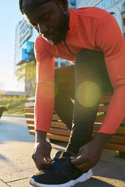 stock image Young male athlete tying shoelace of sneaker while sitting on bench in urban environment agter jogging and bending over leg