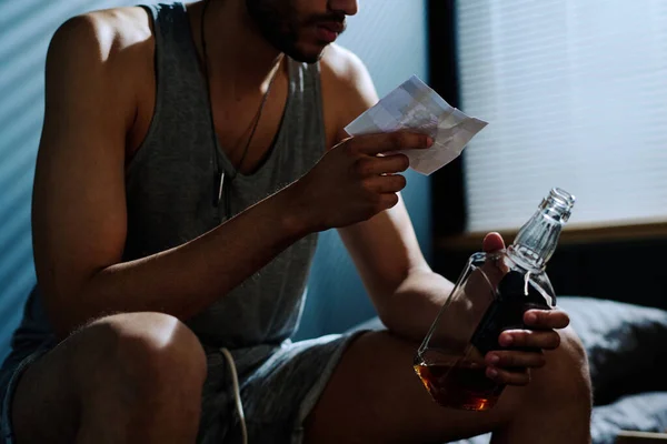 Young depressed man with alcoholic drink looking at picture of him on bike while suffering from post traumatic syndrome and insomnia