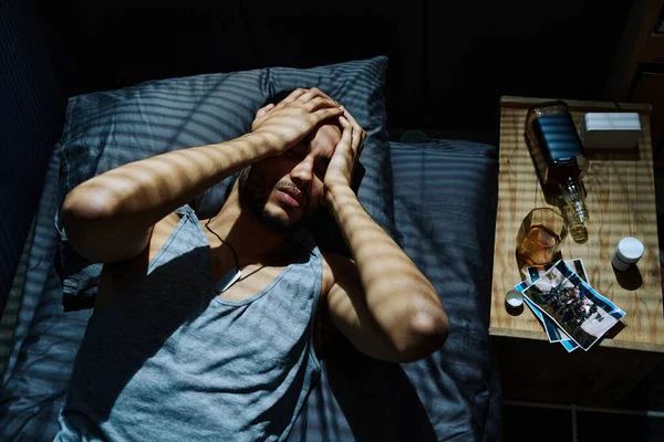 外傷後症候群や障害が原因で頭痛に苦しんでいる若い男がベッドに横たわって手に頭を保持しながら — ストック写真