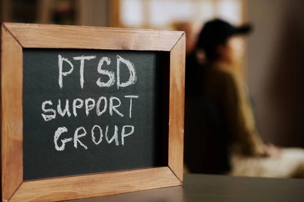 Small chalkboard with name of psychological support group or course in wooden frame standing against attendants of session