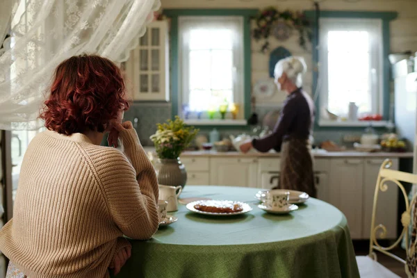 看到穿着针织米色套头衫的小女孩坐在桌旁 端着自制的派 等着她的祖母准备早餐 — 图库照片