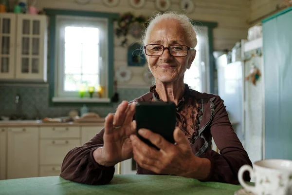 Mulher Sênior Sorridente Óculos Rolando Smartphone Após Café Manhã Enquanto — Fotografia de Stock