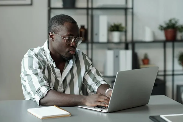 Молодой Серьезный Человек Очках Полосатой Рубашке Глядя Экран Ноутбука Сидя — стоковое фото