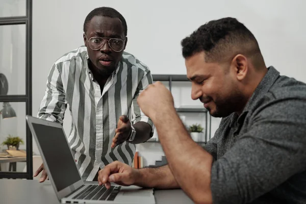若いです怒っているアフリカ系アメリカ人の上司やマネージャーは ノートパソコンの前に座って仕事を終わらせようとするヒスパニック男性の同僚を叱ります — ストック写真