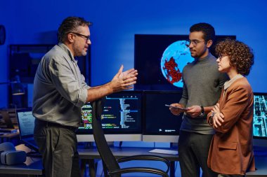 Kendine güvenen olgun patronun sunucu odasında önünde duran genç astlarına çalışma talimatları verirken yan görünüm.