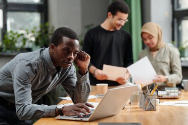 Genç Afrikalı Amerikalı simsar online verileri analiz ederken ya da meslektaşlarına karşı çalışma düzenlerken dizüstü bilgisayarın önünde eğildi.