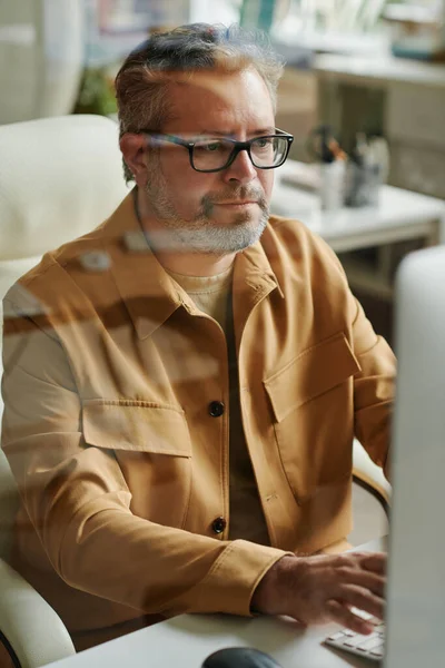 现代成熟的网页设计师或程序员坐在电脑监控器前的桌子旁 一边上网一边看屏幕 — 图库照片