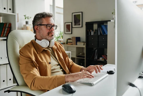 Poważny Siwowłosy Programista Patrzący Ekran Komputera Siedząc Przy Miejscu Pracy — Zdjęcie stockowe