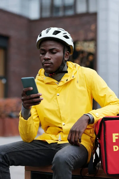 Kasklı Üniformalı Genç Afrikalı Teslimatçı Dışarıdaki Akıllı Telefondan Online Müşterilerin — Stok fotoğraf