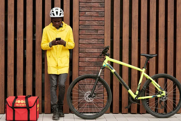 Junger Afroamerikanischer Kurier Uniform Steht Hauswand Und Blättert Smartphone Während — Stockfoto