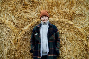 Modern çiftliğin genç ve mutlu kadın çalışanı günlük giysiler içinde büyük bir samanlıkta duruyor. Kuru kamışla sarılmış ve kameraya bakıyor.