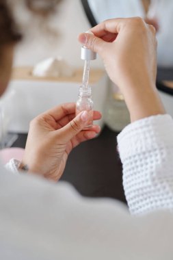 Elinde gençleştirici serumla küçük bir kavanoz tutan genç bir kadının elleri. Ya da yüzüne kozmetik ürünler sürerken yağ ve damlatıcının özü.