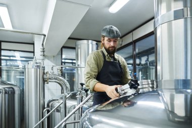 Küçük bira fabrikası işçisi mayalanan biralarla tankları kontrol ediyor.