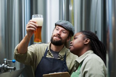 Gülümseyen bira fabrikası işçileri bira köpüğünün kalınlığını kontrol ediyor.