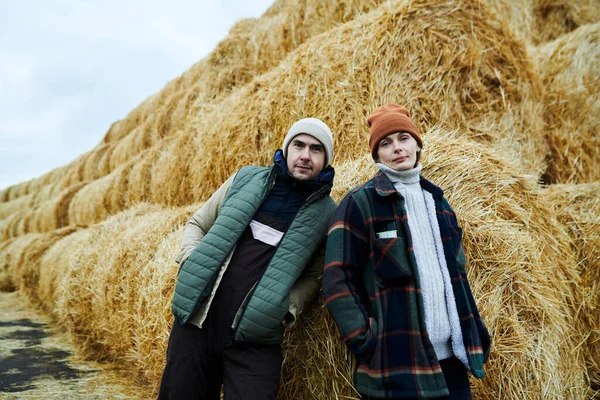 两个年轻自信的农场工人穿着便服 站在乡间大堆新鲜干草旁边看着相机 — 图库照片