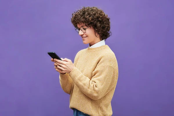 穿着眼镜和米色套头衫 站在紫色背景下的快乐的年轻黑发女人的侧视图 — 图库照片