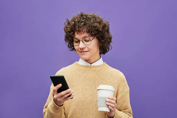 穿着休闲装的年轻黑发女人 用智能手机浏览网上新闻 喝着紫色背景的咖啡 — 图库照片