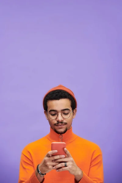 오렌지 색옷을 남자가 라벤더 배경에 맞서서 스마트폰으로 메시지를 보내는 — 스톡 사진