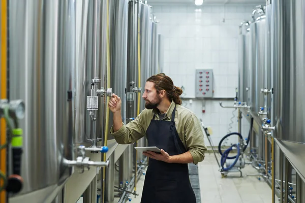 啤酒厂工人检查每个装有啤酒的罐体的压力指示器 — 图库照片