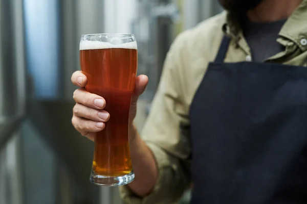 マイクロブルワリーで生産されるビールの大きなガラスを持つ労働者 — ストック写真