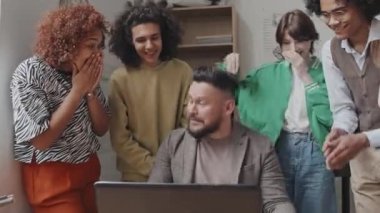 Çok ırklı lise öğrencilerinin el çırpması, sınıfta oturan erkek öğretmenin etrafında dikilmesi, öğleden sonra laptopta sınav sonuçlarını kontrol etmesi.