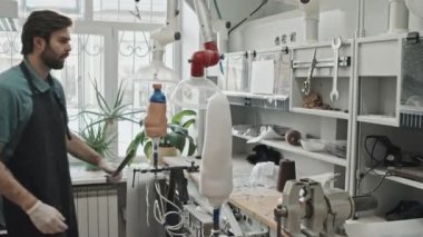 Sakallı, önlük takmış, insan kalçası alçısına protez bacağı takan genç, beyaz bir adam.