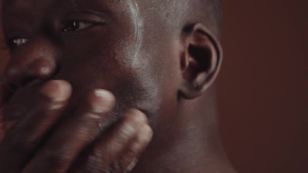 演播室特写 年轻英俊的黑人青年男子在他的脸上撒满了滋养或保湿的乳霜 动作缓慢 — 图库视频影像