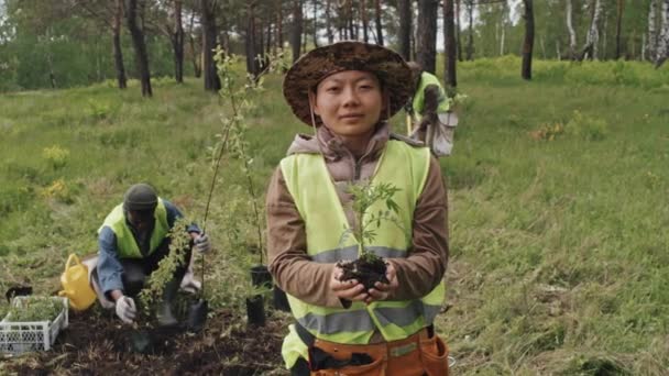 Średni Portret Azjatyckiej Ogrodniczki Zielonej Kamizelce Odblaskowej Sadzonką Patrzącej Kamerę — Wideo stockowe