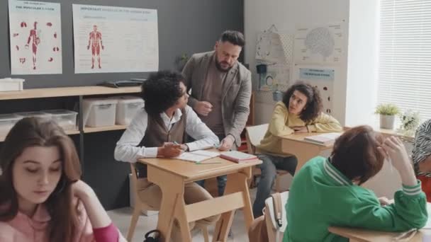 跟踪观察留胡子的男教师 帮助早上坐在课桌前上解剖学课的青少年 — 图库视频影像
