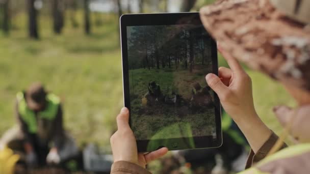 Przez Ramię Osoby Nierozpoznawalnej Korzystającej Tabletu Robiącej Zdjęcia Ogrodnikom Sadzącym — Wideo stockowe