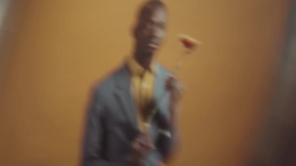 身穿灰色西装 黄衬衫 手持鲜花 望着相机的年轻非裔美国人的水平画室肖像 — 图库视频影像