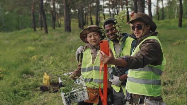Średnie Trzech Różnych Ogrodników Zielonych Kamizelkach Robiących Selfie Smartfonie Lesie — Wideo stockowe