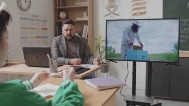 Erkek beyaz öğretmeni sınıfında otururken izlemek, konuşmak, öğleden sonra arılar hakkında eğitici bir film göstermek.