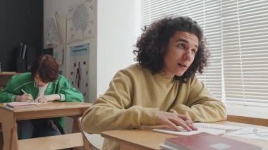 Kıvırcık, kıvırcık, çift cinsiyetli adamın düşük açılı göğsü. Ders masasında oturuyor, el kaldırıyor ve öğleden sonra sorular soruyor.
